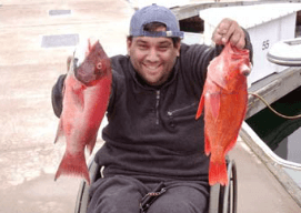 Man in wheelchair holding up 2 fish